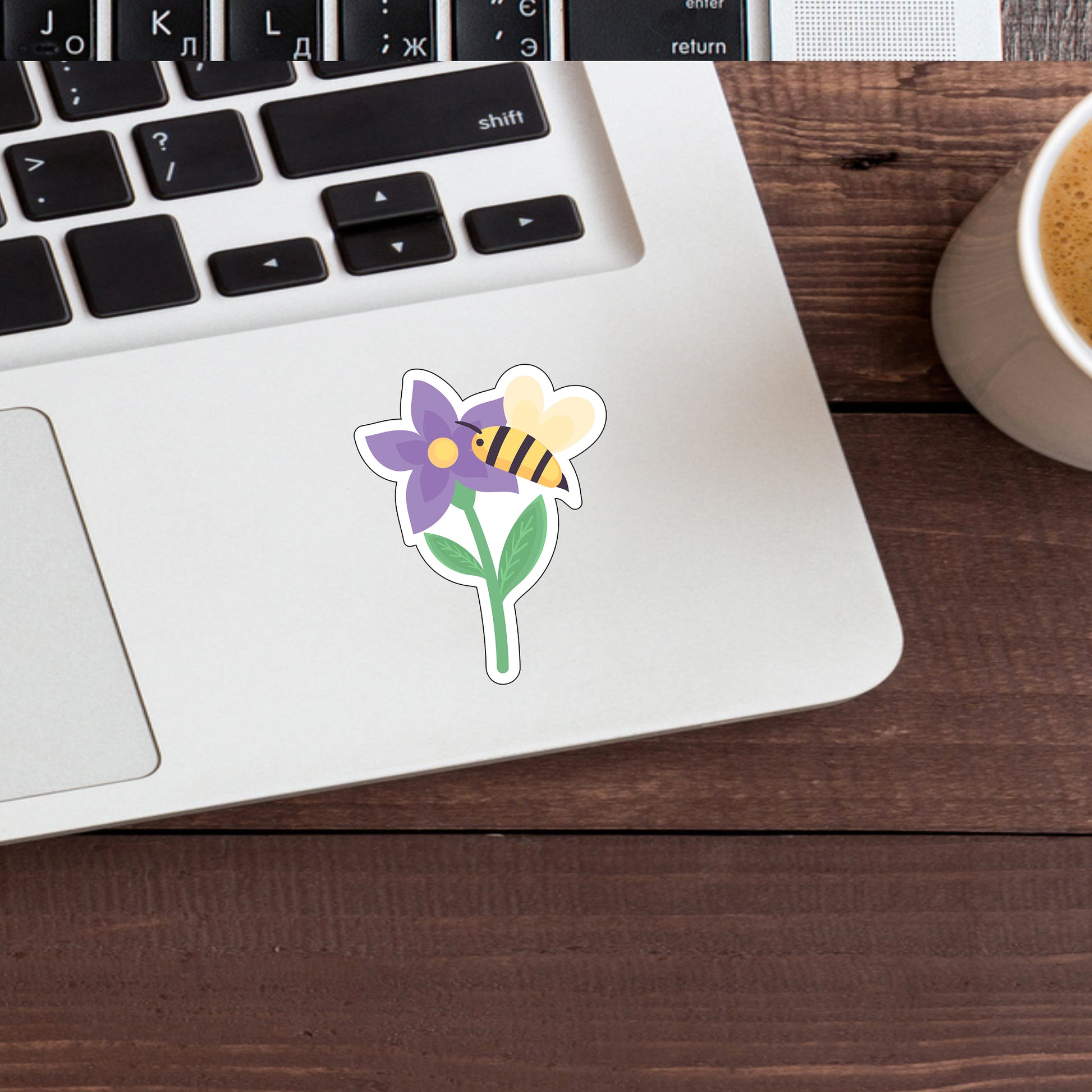 a cup of coffee next to a laptop with a sticker of a flower